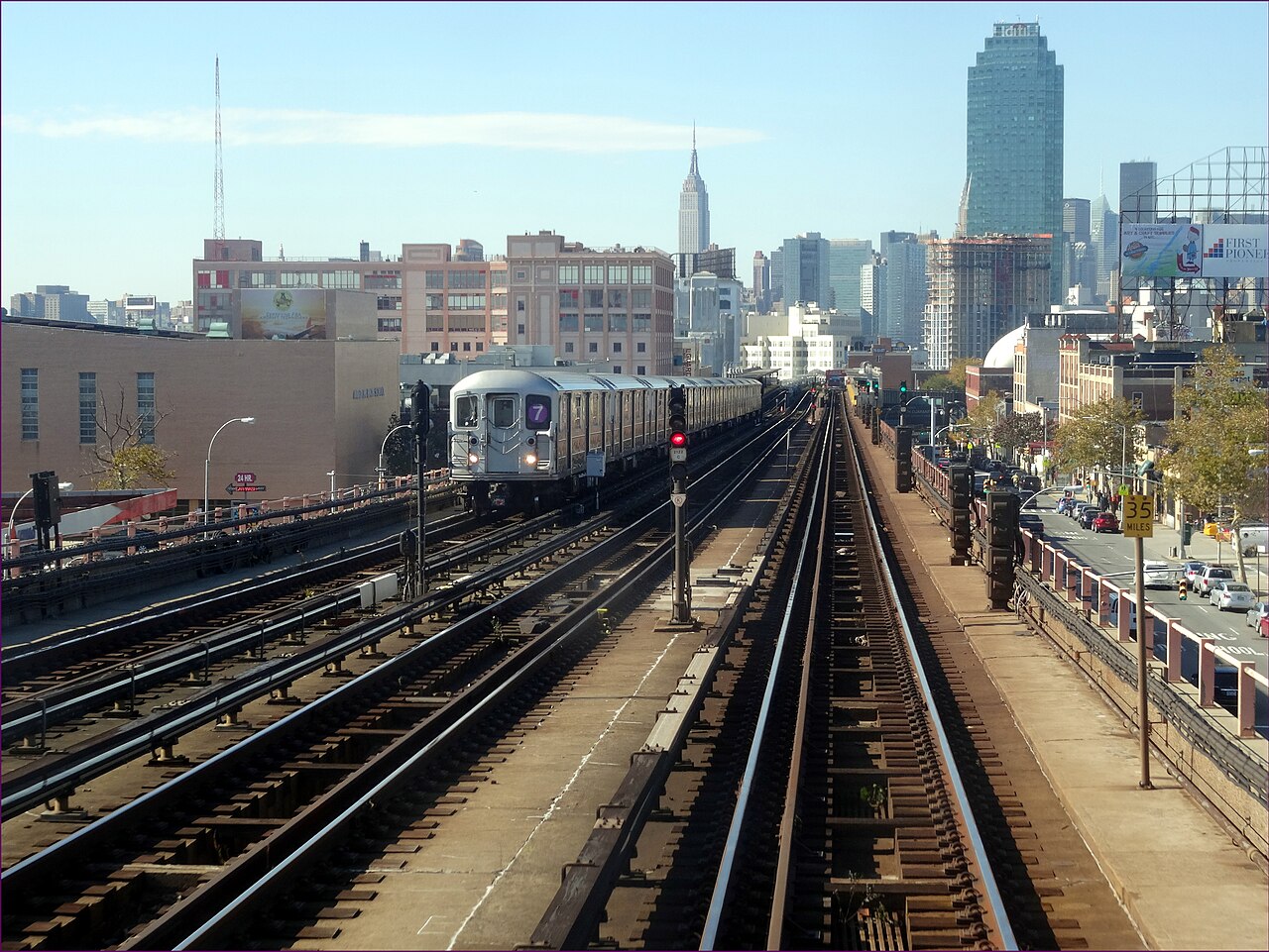 A 7 train on elevated tracks in Queens, with the Manhattan skyline beyond.